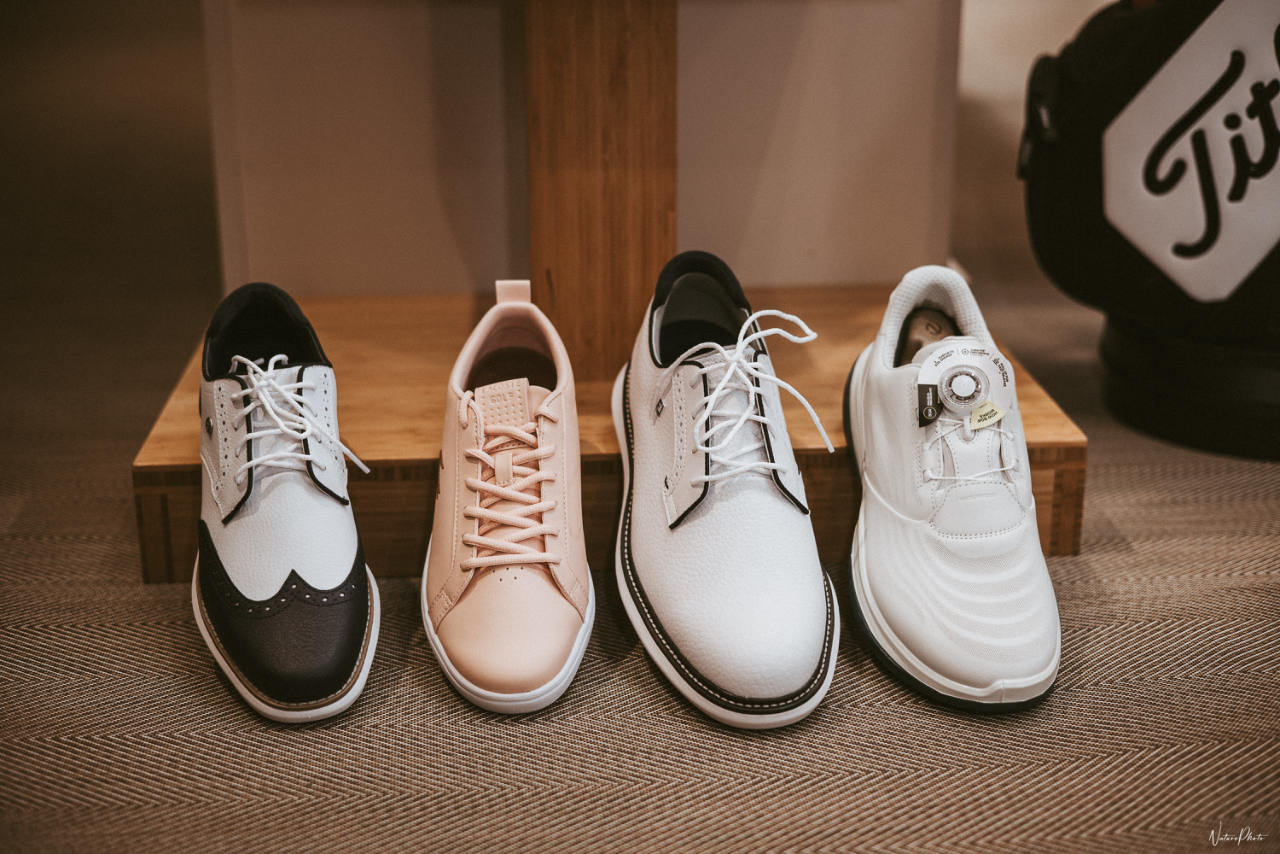 Quatre paires de chaussures de golf alignées sur un présentoir en bois