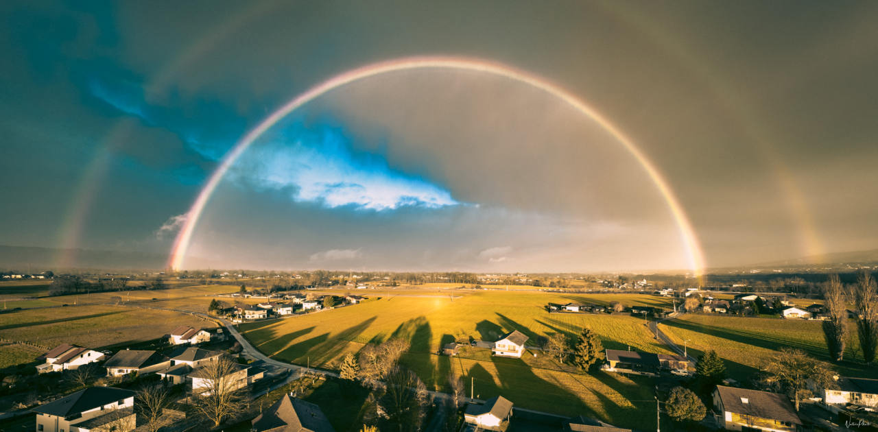 Vue aérienne d’un double arc-en-ciel au-dessus d’un village et des champs