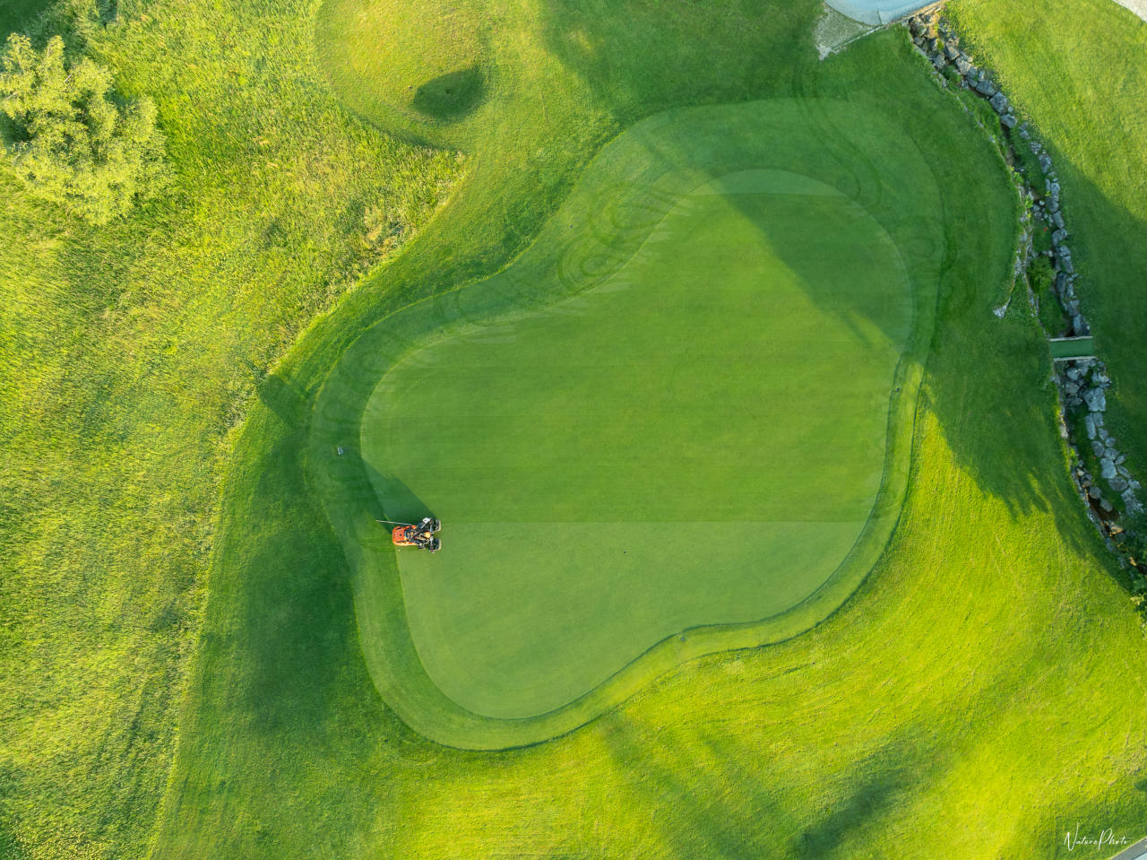Green de golf vu à la verticale depuis un drone, une tondeuse au bord
