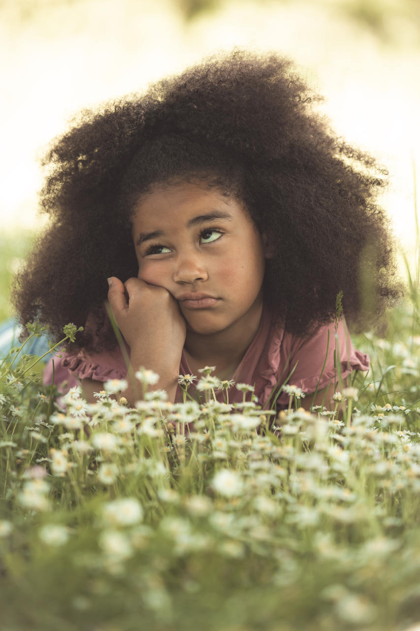 Fillette aux cheveux bouclés, le menton dans la main, allongée dans les fleurs