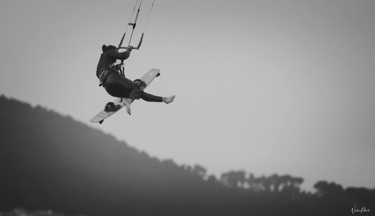 Kitesurfeur suspendu en l’air au-dessus d’une colline, en noir et blanc