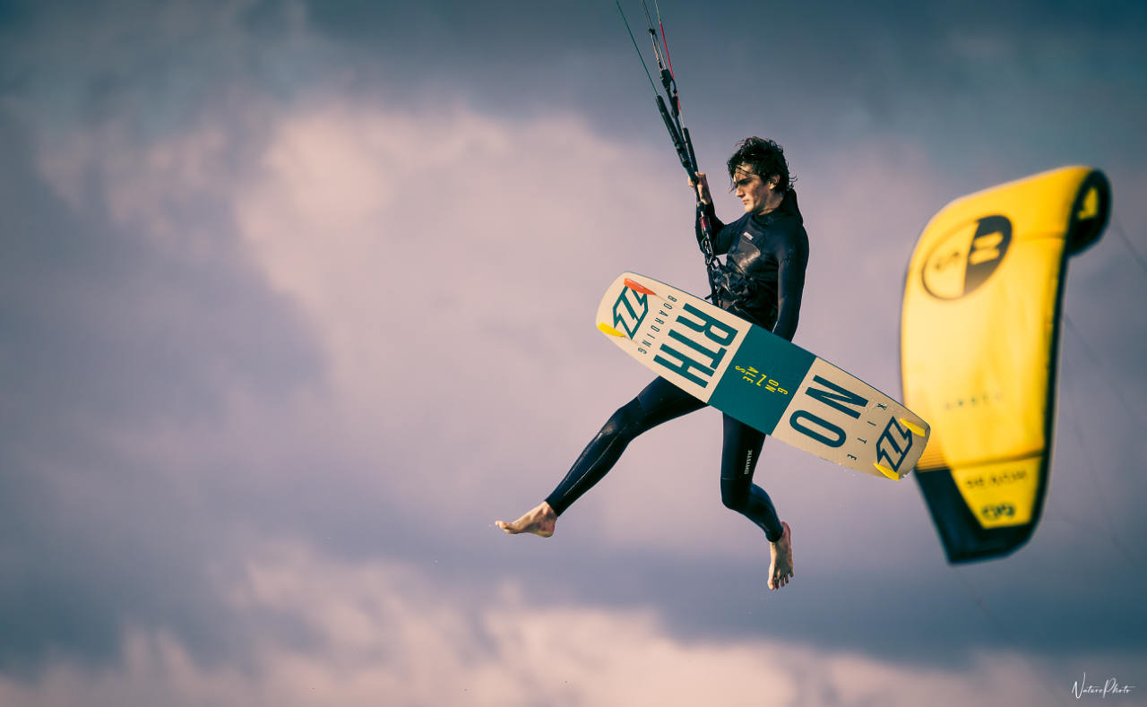 Kitesurfeur en plein saut, planche tenue à la main, devant son aile jaune