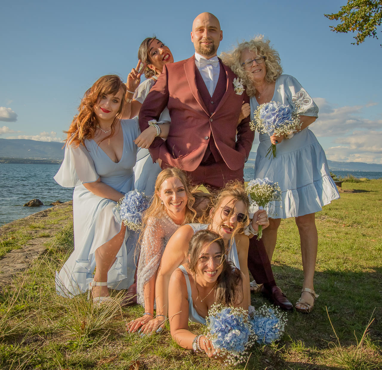 Le marié entouré des demoiselles d’honneur en robes bleu pâle, au bord d’un lac