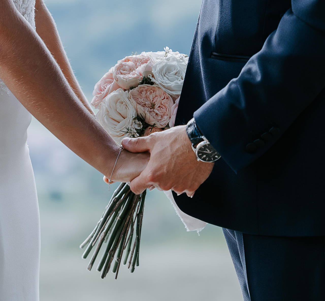 Les mains des mariés jointes autour d’un bouquet de roses pâles
