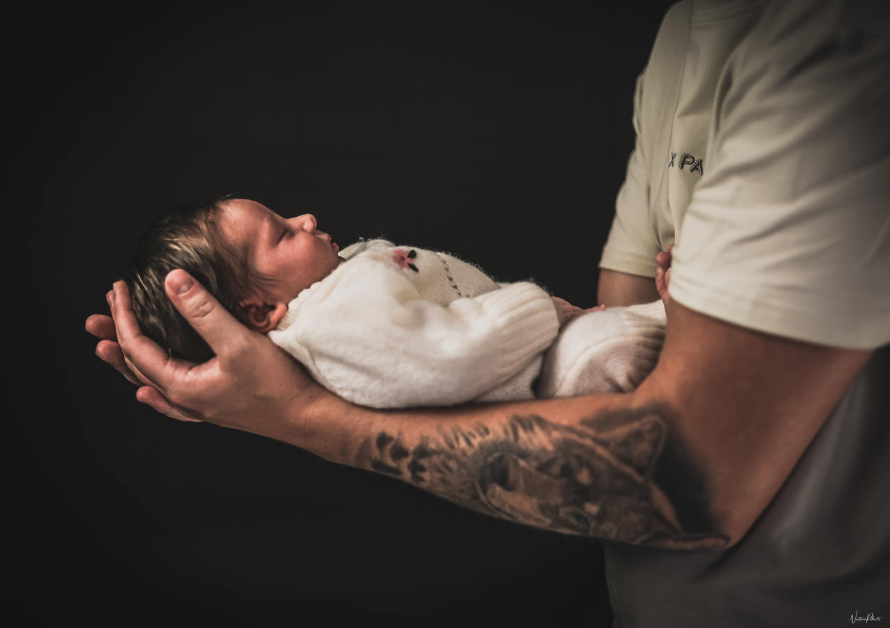 Nouveau-né endormi dans les bras tatoués de son père, sur fond sombre
