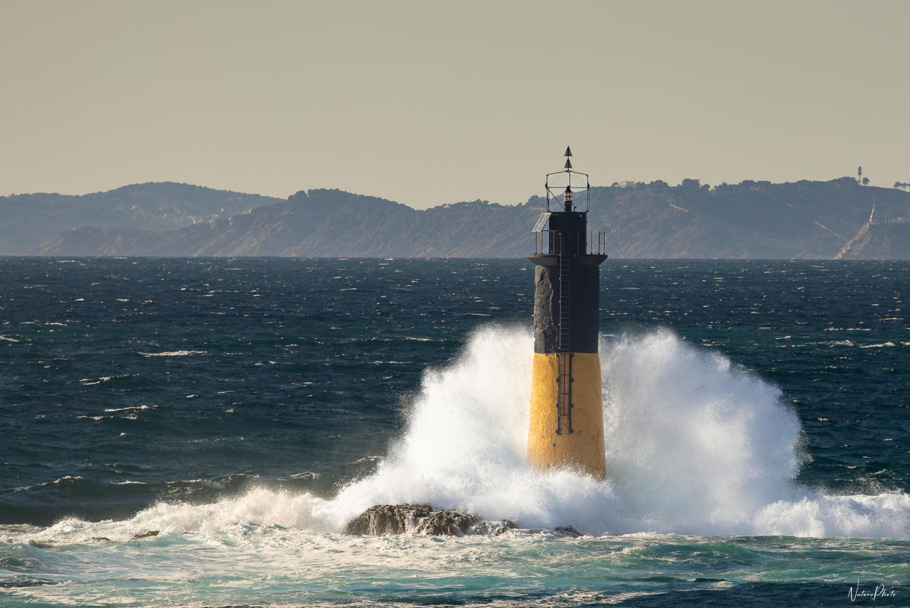 Vague qui se brise sur un phare jaune et noir en mer