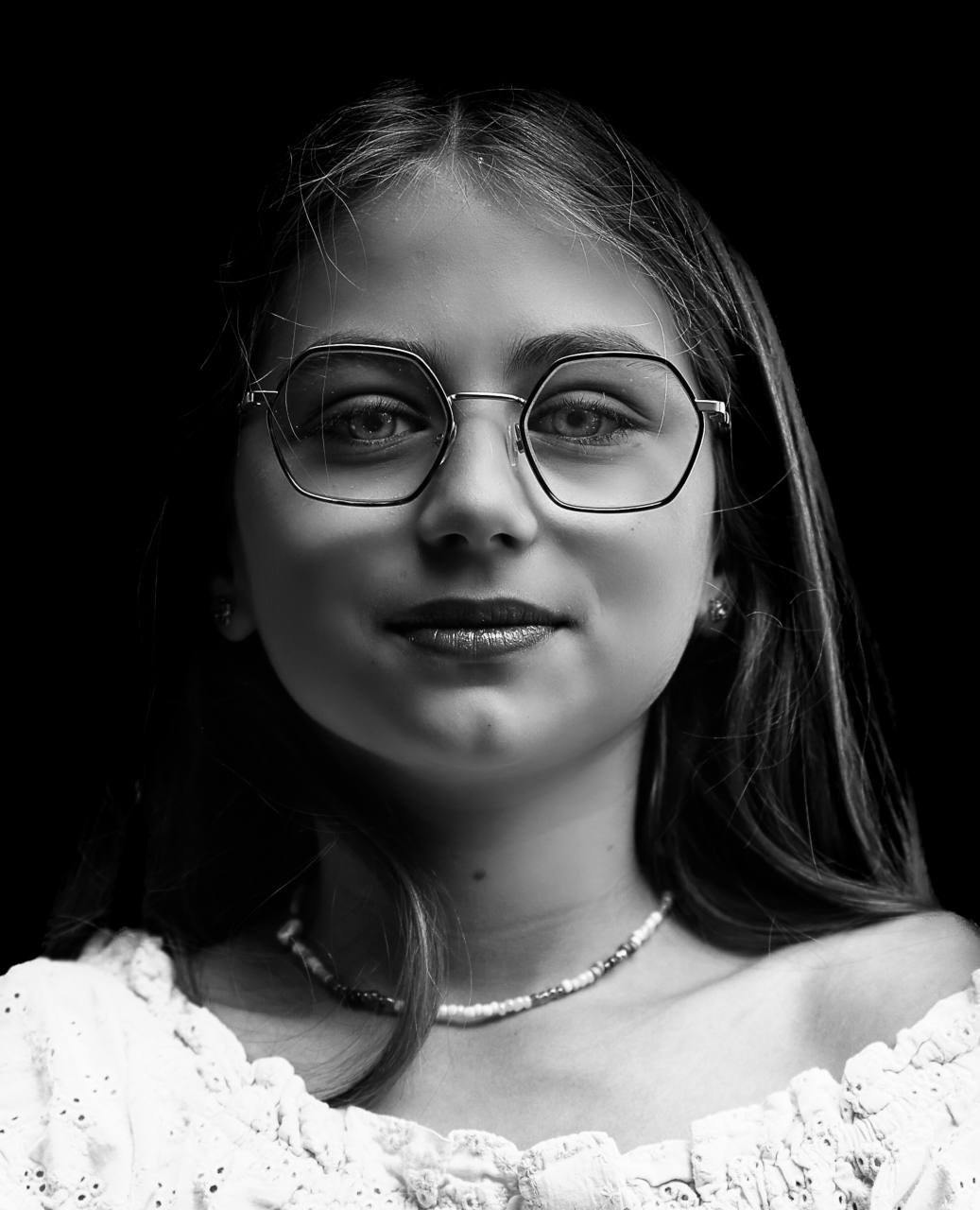 Portrait en noir et blanc d’une adolescente à lunettes, sur fond noir